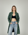 Woman wearing a green Kashmiri embroidered wool blend Kashmiri jacket, black top, and blue jeans on a gray background