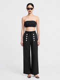 A model wearing a black strapless bandeau crop top and matching black wide-leg trousers with white decorative buttons, styled with black sunglasses and sandals against a light gray studio background. ishq e amore